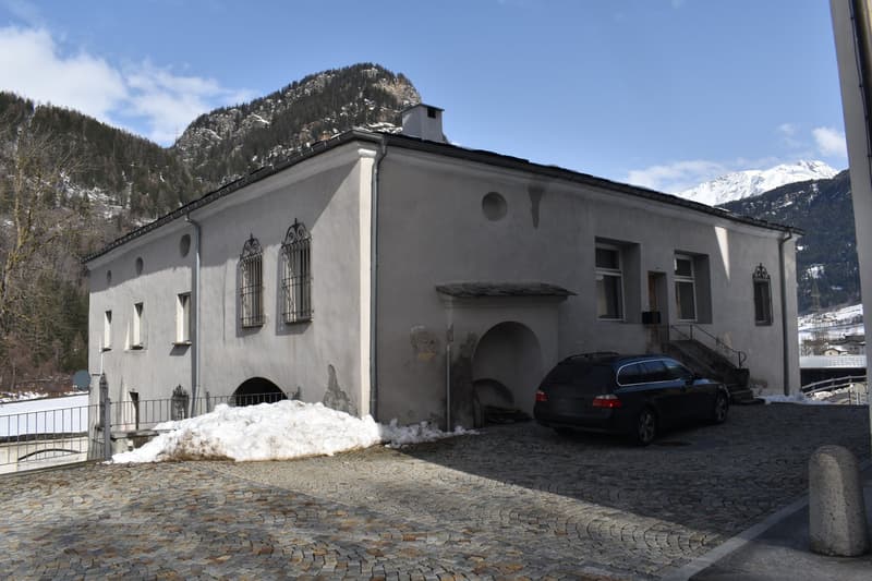 grey house with windows, arch entrance, snow covered ground, mountains in background