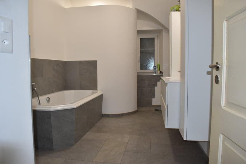 bathroom with bathtub, sink, window, tiled floor, curved wall