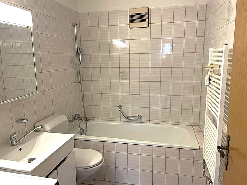 Bathroom with white tiles, bathtub, toilet, sink, mirror, and towel rack.