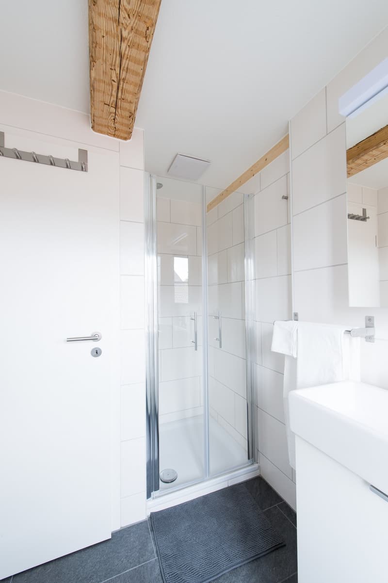 White tiled walls, glass shower enclosure, towel rack, wooden ceiling beam