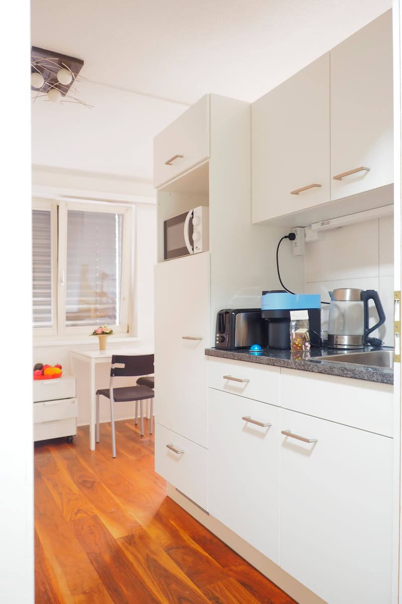 White cabinetry, granite countertop, microwave, sink, toaster, coffee maker, kettle, wooden floor