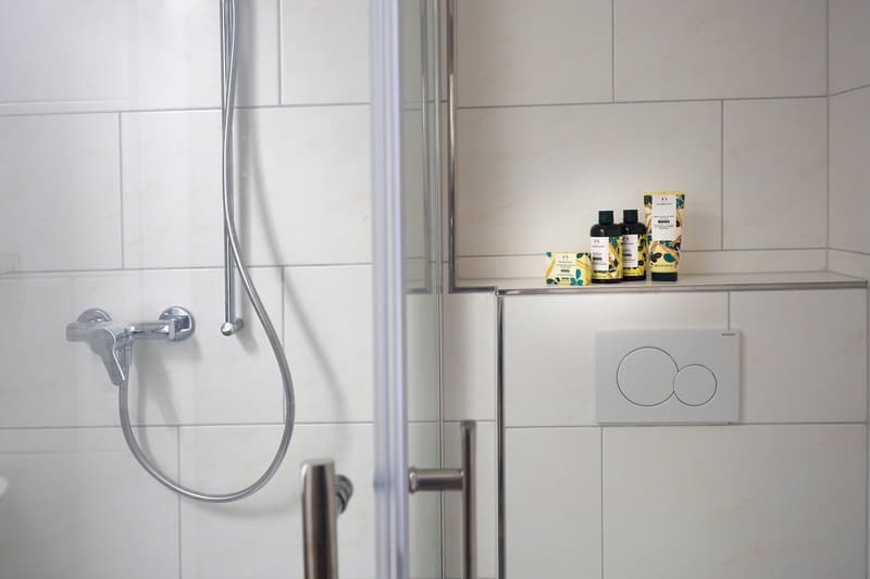 modern bathroom with shower, tiled walls, shampoo bottles, clean shower hose