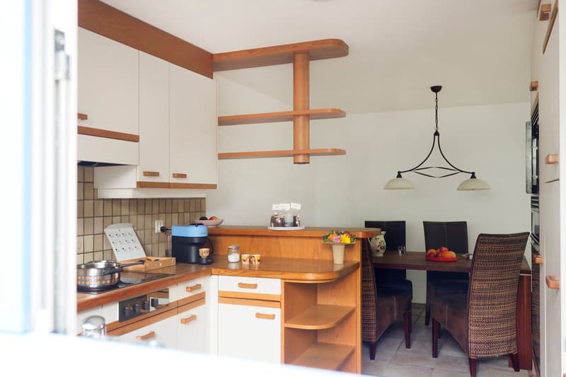 Wooden countertops, white cabinets, hanging shelf, dining area with table and chairs, pendant light, oven, gas stove, coffee machine, power outlet