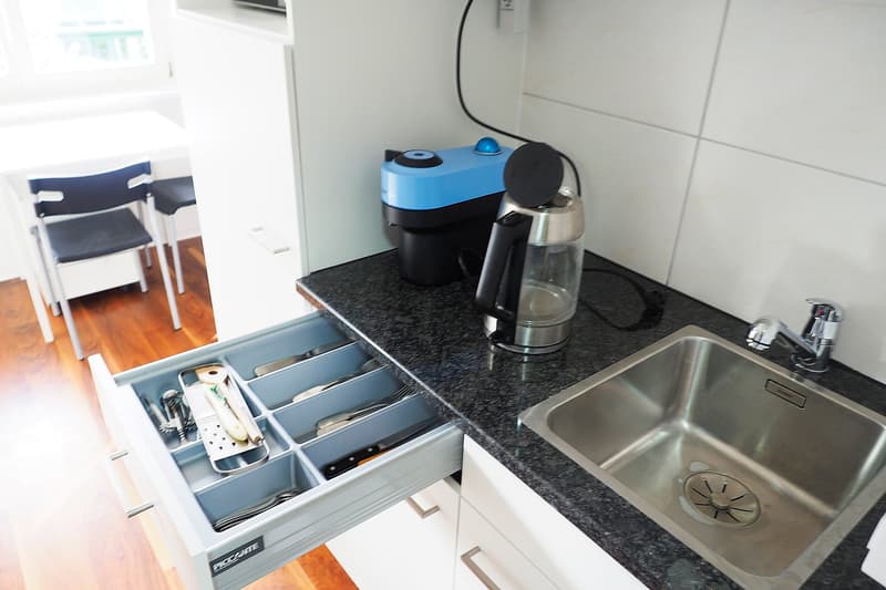 modern kitchen, dark countertop, silver sink, open drawer with cutlery, water jug and coffee maker