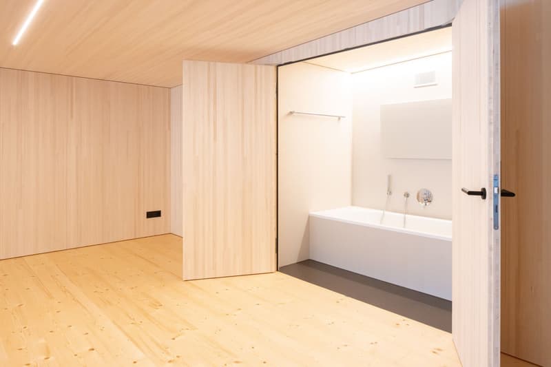 a bathtub, a wooden wall, a door, an open door, a wooden floor, and a light on the ceiling