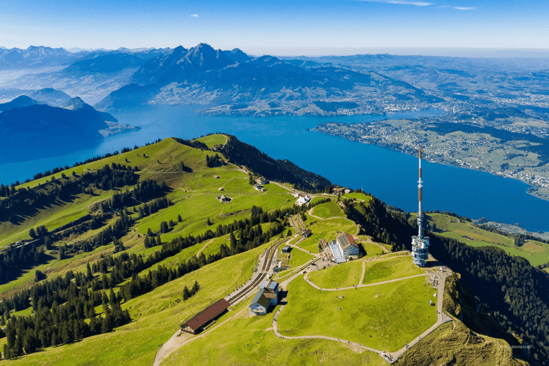 mountain with green grass, lake, forest, small buildings, tower