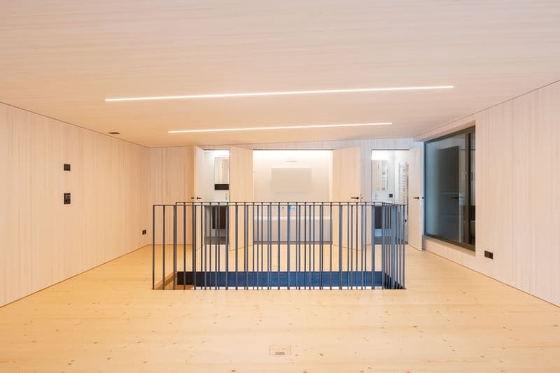 Open space with wooden floor, white walls, metal railing, and a bathtub in the center