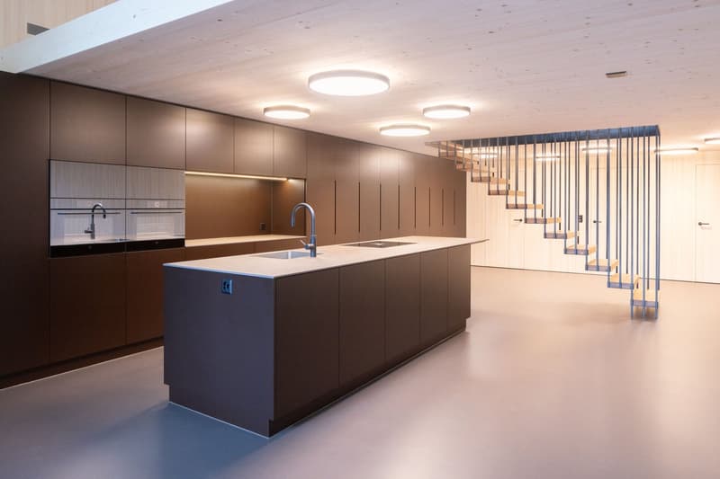 modern kitchen with island, wooden cabinets, stainless steel sink, faucet, built-in appliances, round ceiling lights, staircase