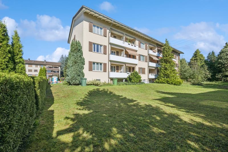 4 story building, beige walls, brown shutters, balconies, green trees, bushes, lawn