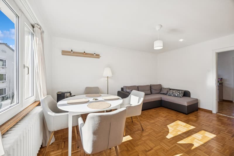 white walls, wooden floors, white dining table, couch, lamp, radiator, open window with view