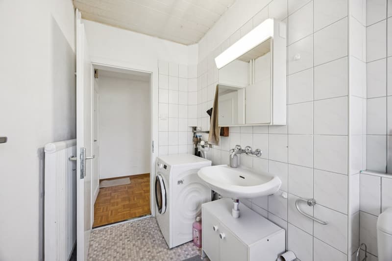 White tiled bathroom with a sink, washing machine, and a radiator.