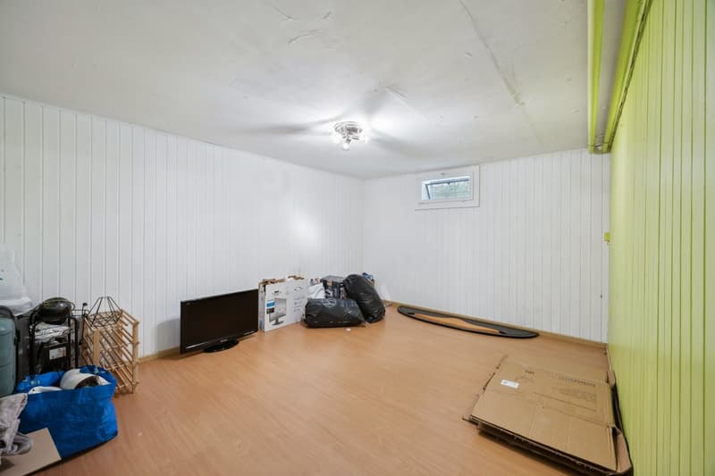 empty room with white and green walls, wooden floor, a small window, ceiling light, and various items on the floor