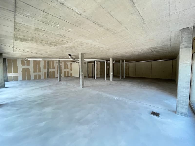 Empty room with concrete floor, walls, and ceiling, several pillars, unfinished walls, and pipes