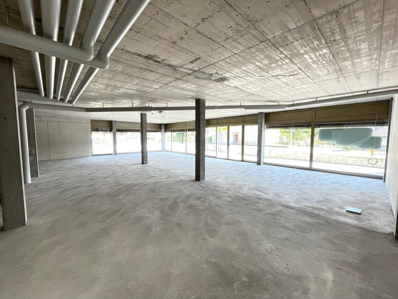 Empty room with concrete floor, large windows, and exposed pipes on the ceiling