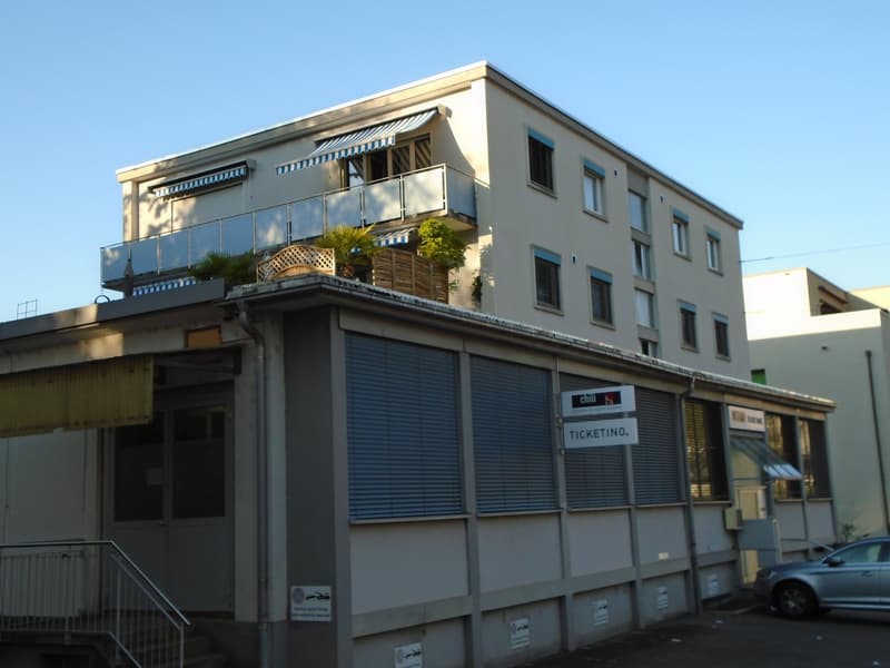 multistory building, rooftop balcony, entrance, sign reading 'TICKETINNO', potted plants, gray exterior, glass doors