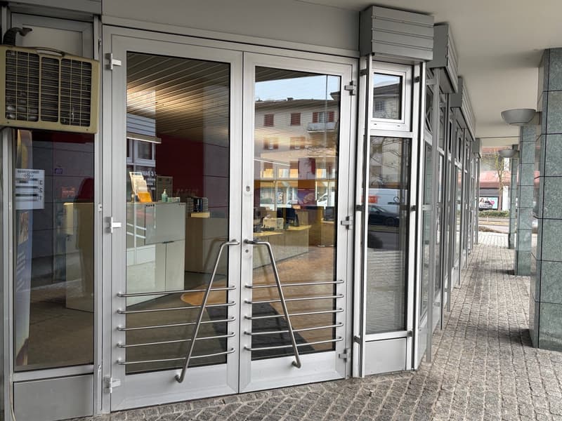 commercial building with glass doors and windows, air conditioning unit mounted on the wall, metal handrails, tiled walkway