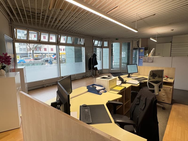 an office room with multiple desks, computer monitors, keyboards, mice, printers, glass windows, and cabinets