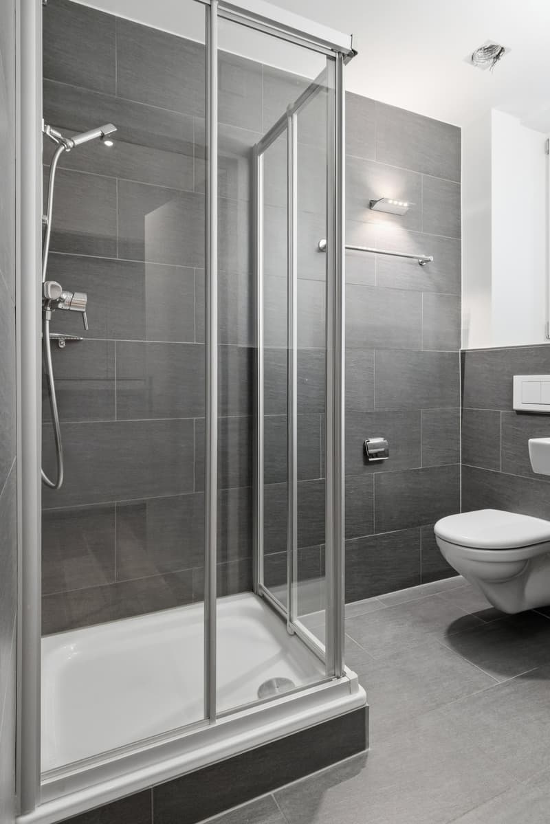 modern bathroom with glass shower, white toilet, gray tiles, silver fixtures