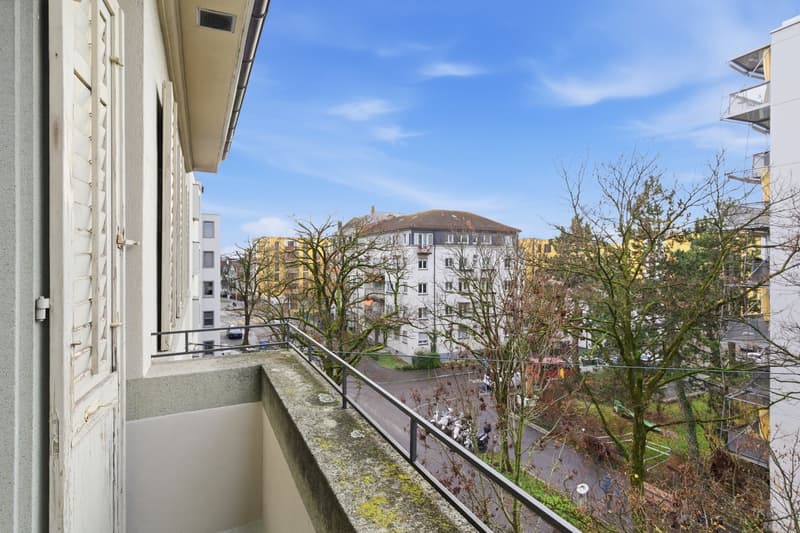 Balcony with metal railings, overlooking a street with trees and buildings