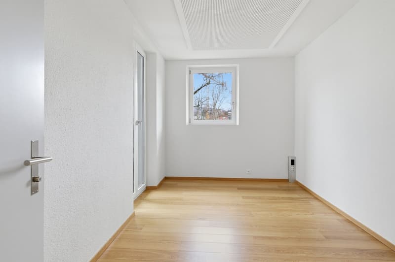 Empty room with white walls, wooden floor, glass door, small window, and a power outlet.