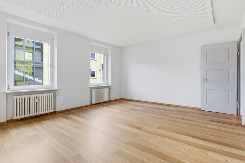 empty room, wooden floor, white walls, two windows, radiators, open door