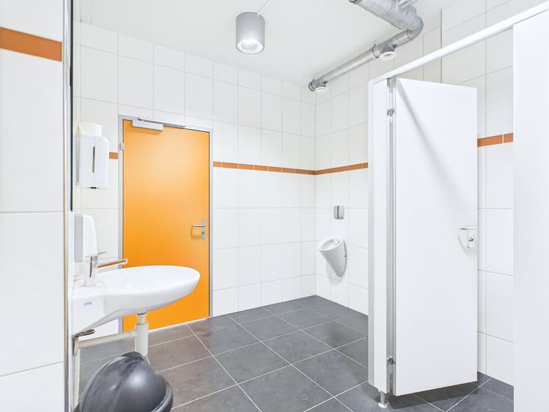 Tiled bathroom with white walls, orange accent wall, sink, urinal, and shower stall