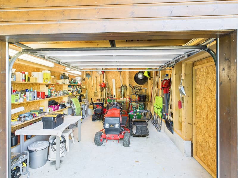 Garage with lawnmowers, shelves, tools, buckets, and a red tractor