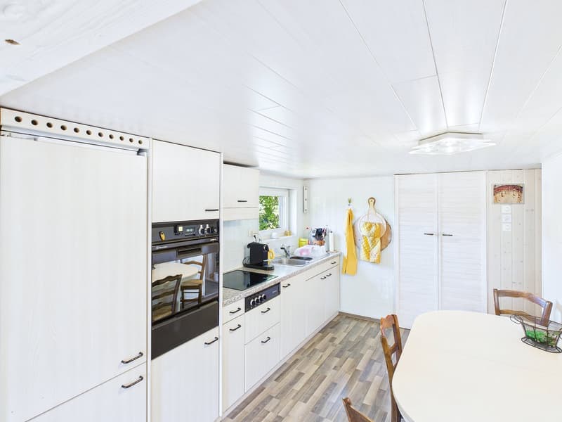 modern kitchen with white cabinetry, black oven and stovetop, dining table and chairs, round ceiling lamp