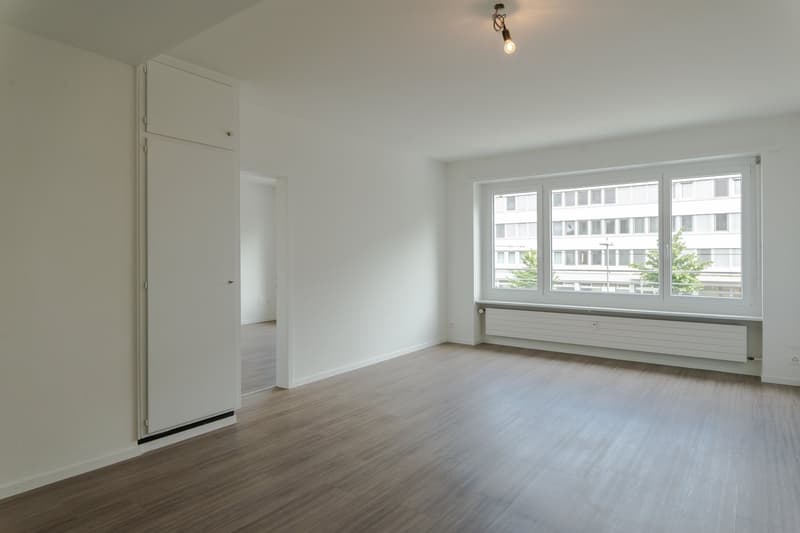 empty room, white walls, wooden floor, large window, white radiator