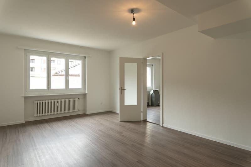 empty room, wooden floor, white walls, large window, radiator, open door