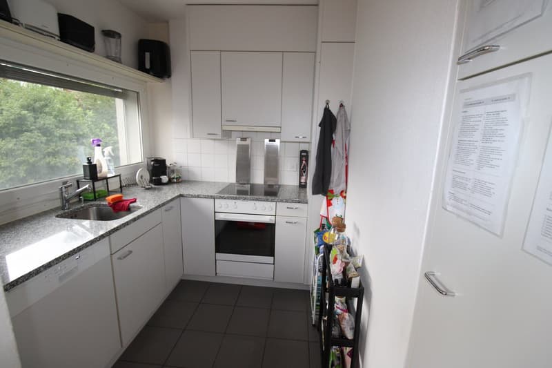 White cabinetry, granite countertops, gas stove and oven, stainless steel sink, dishwasher, large window, power outlet, hanging clothes, white tiled walls.
