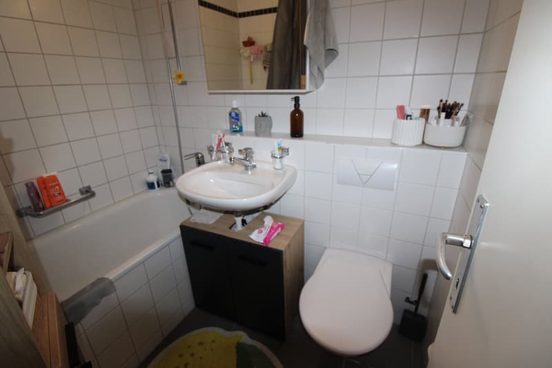 white bathroom, bathtub, sink, toilet, white tiles, mirror, bathroom items on shelf