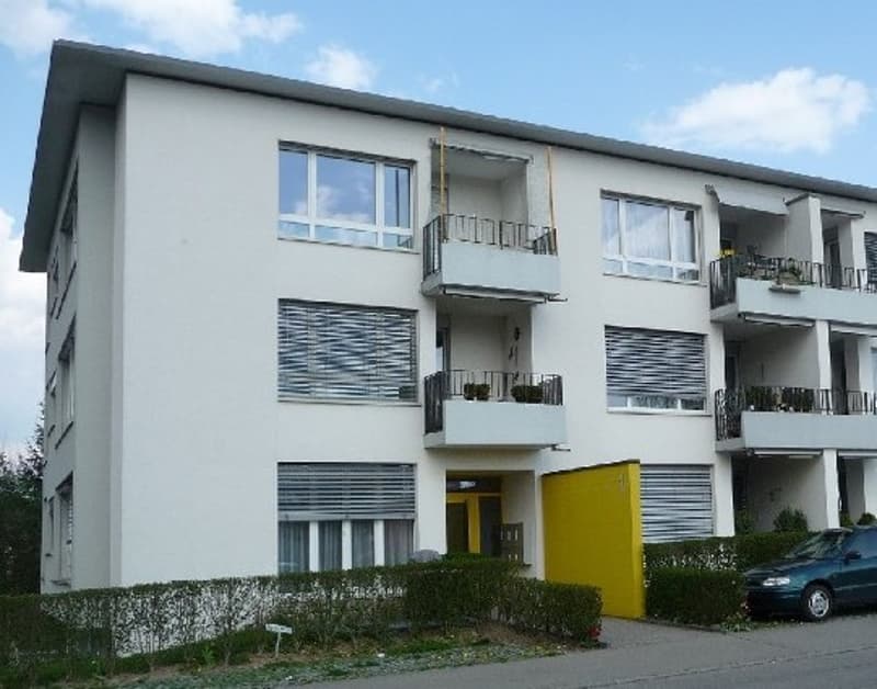 4-story building, white exterior, windows, yellow front door, car parked in front, hedges