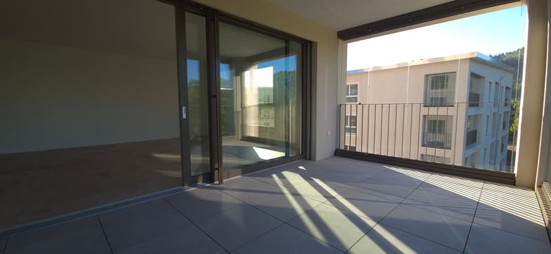 Balcony with sliding glass doors, tiled floor, metal railing, view of another building and trees