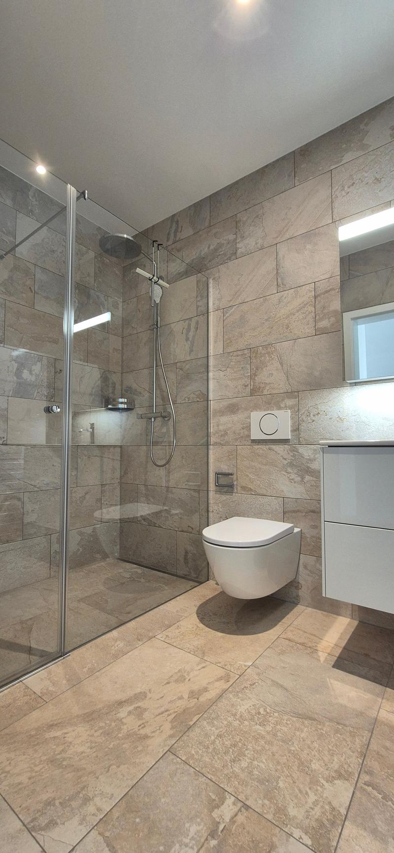 modern bathroom, glass shower enclosure, white toilet, white vanity, tiled walls, built-in mirror