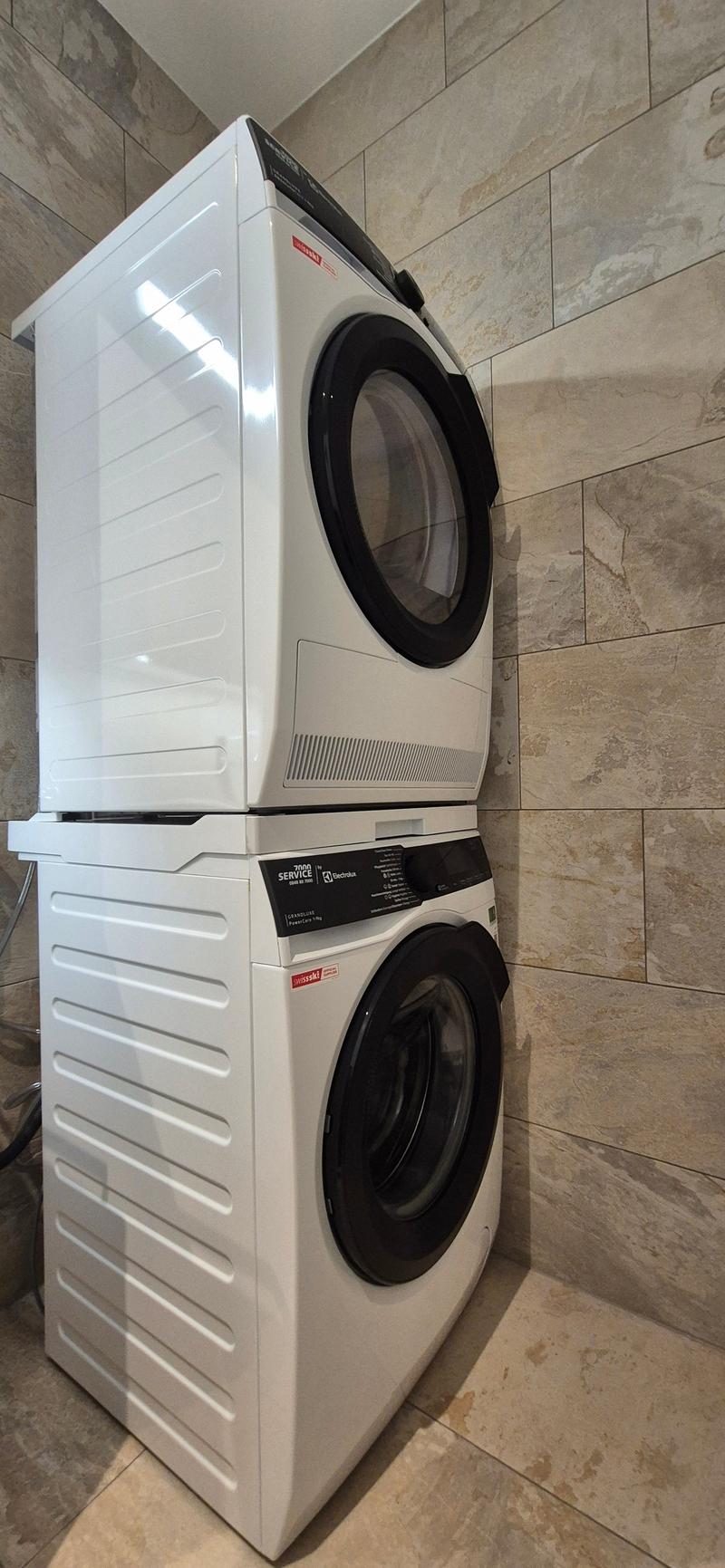 A white washing machine and dryer stacked on top of each other in a room with tiled walls.