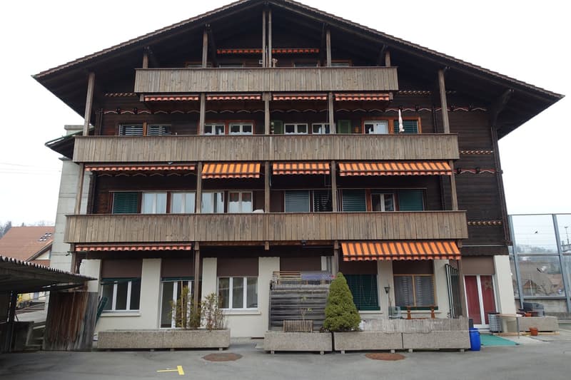3-story wooden chalet-style building with balconies, decorative wooden trim, and awnings