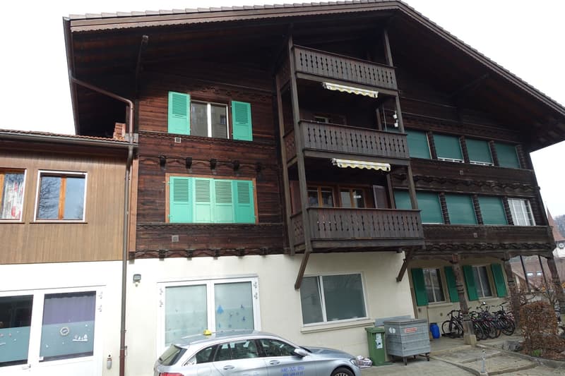 2-story wooden chalet-style building with green shutters, balconies, and a covered porch area. There are bicycles parked in front of the building.