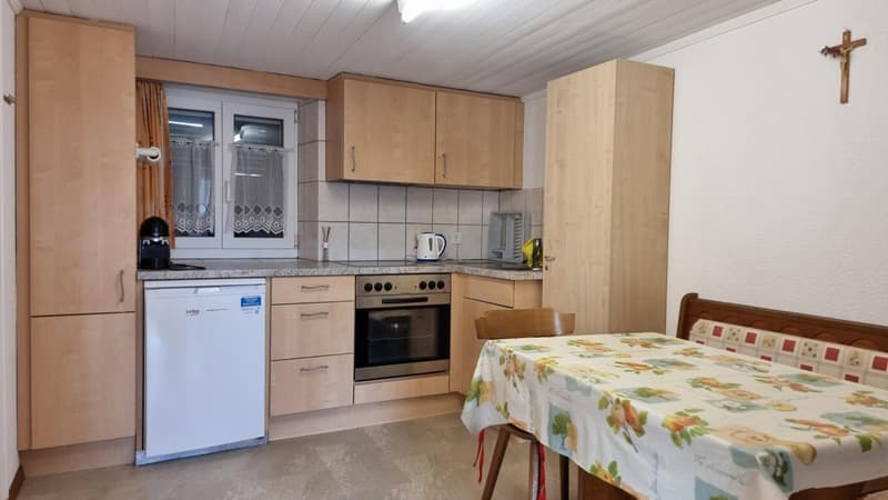 Fully equipped kitchen with wooden cabinets, tiled backsplash, stove, oven, dishwasher, and washing machine. Dining table with floral tablecloth in the corner.