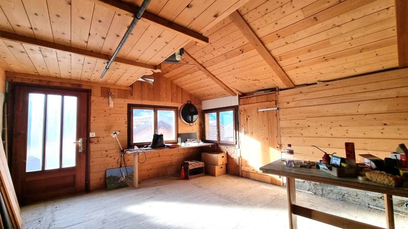 Wooden cabin interior with exposed wood beams and paneling, large windows, desk, and storage boxes