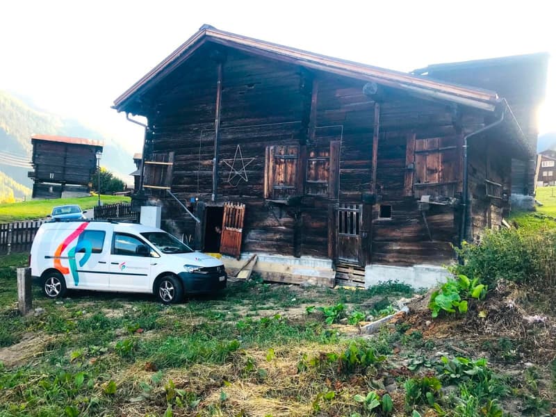 Wooden chalet, red roof, wooden doors, white van parked in front, mountainous landscape