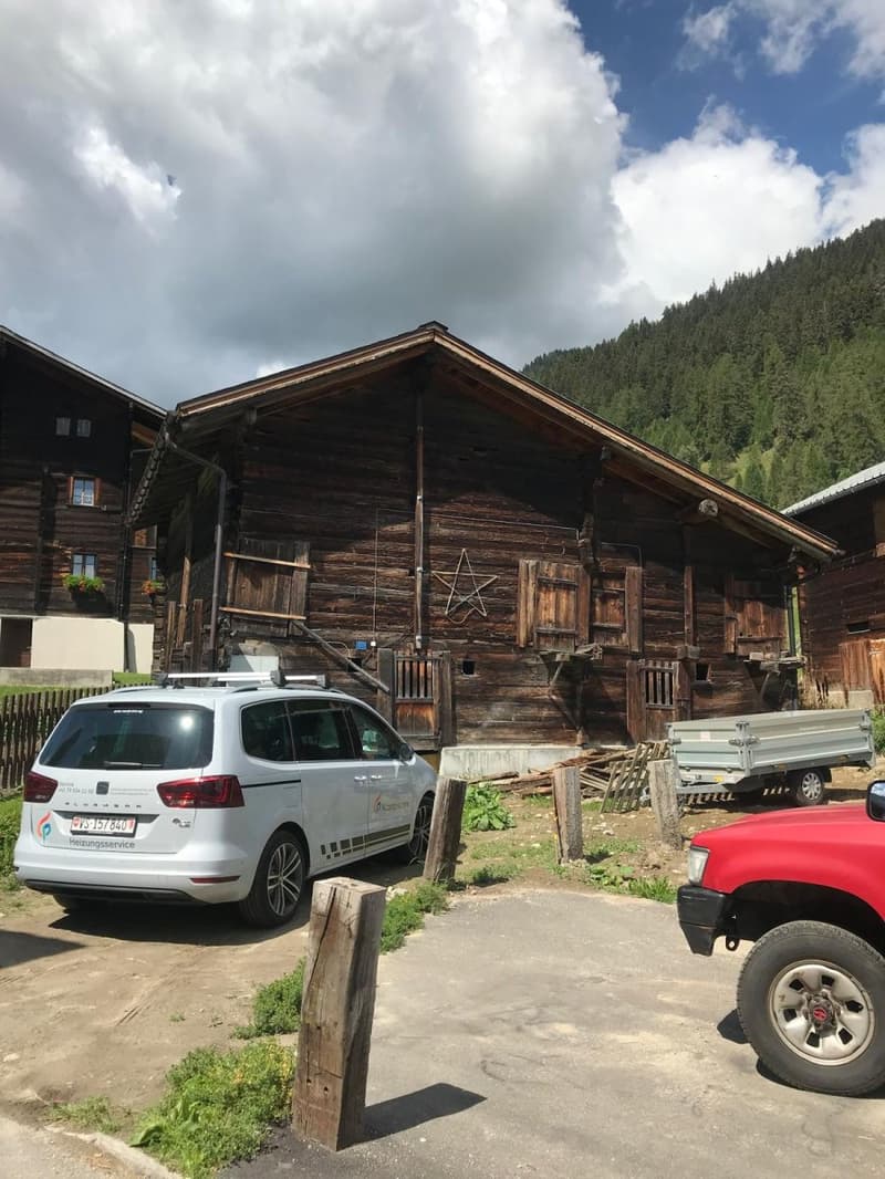old wooden house, parked cars in front, mountainous landscape in the background