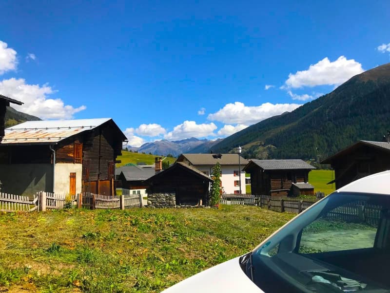 Traditional wooden houses, rocky hill background, green grass, clear sky, white clouds, streetlight, parked white van