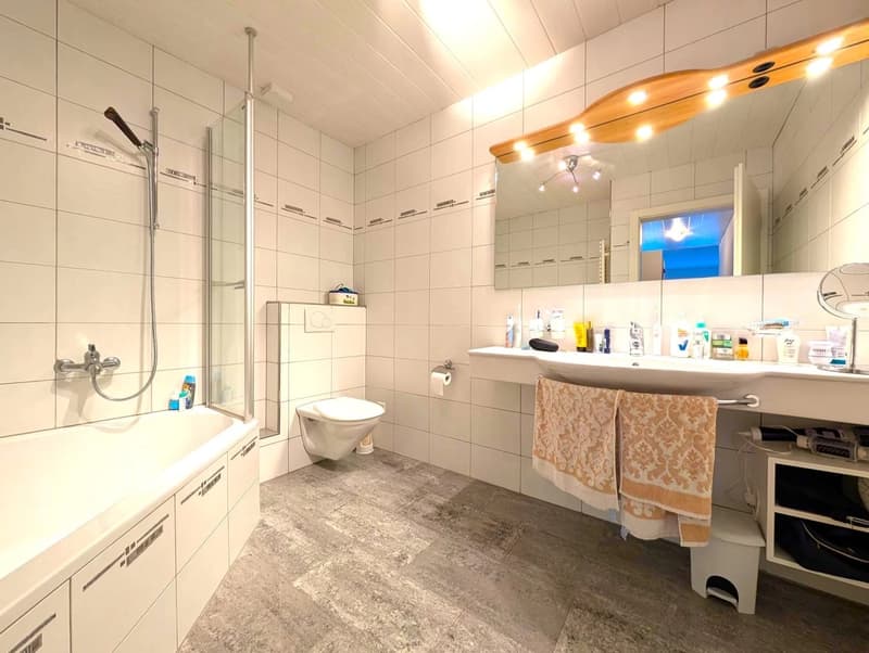 Large bathroom with tiled walls, shower stall, toilet, vanity sink with mirror, and shelves for storage. The bathroom also has a private washing machine.