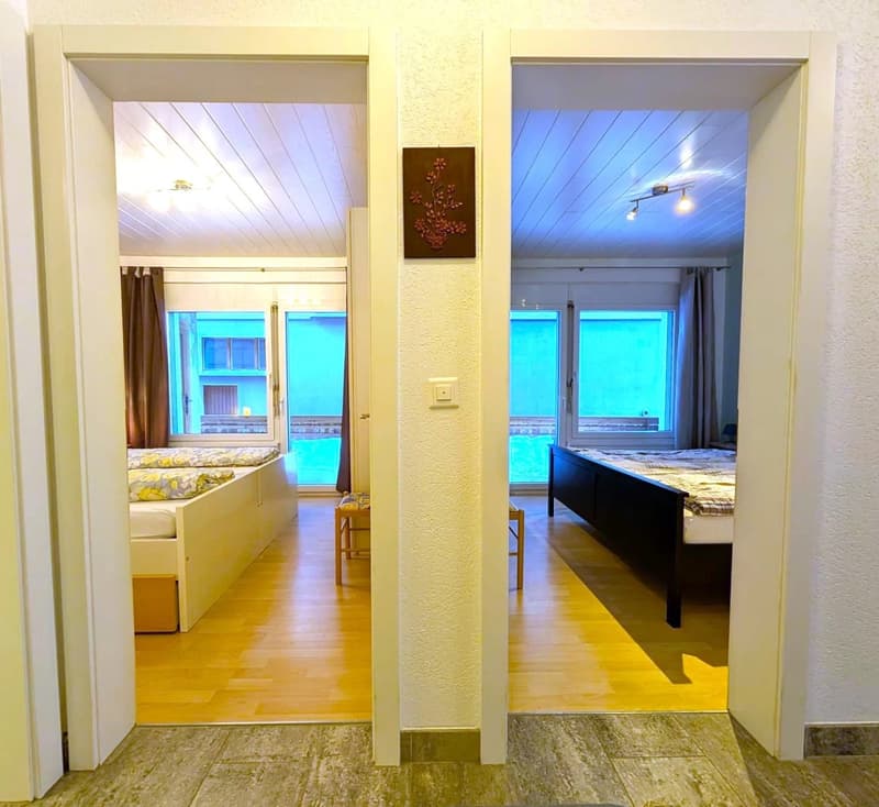 2 beds, wooden floor, white walls, large windows, pool view, storage box, wooden benches, bedside table with lamp