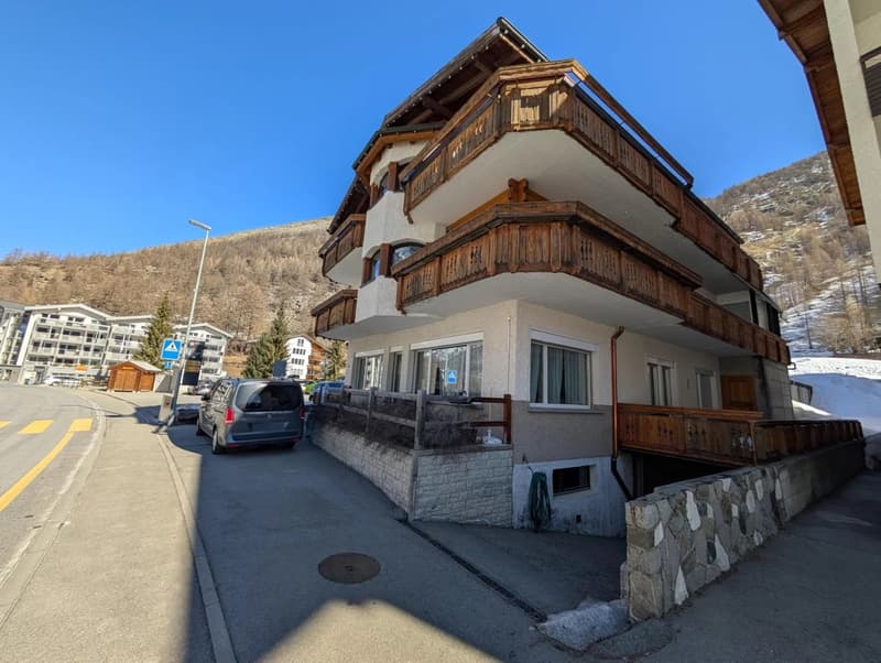 4 story building, wooden balconies, white exterior, stone retaining wall, mountain backdrop