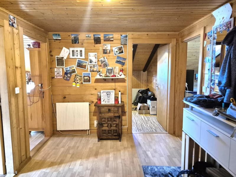 Cozy wooden cabin interior with a wall covered in photos and artwork, a wooden cabinet, and a blue cabinet. The room has a wooden ceiling and floor.