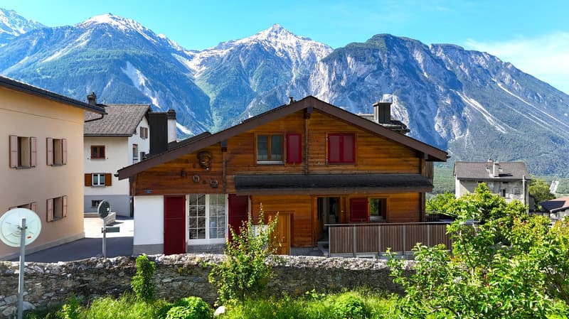 Alpine style wooden house, red shutters, mountains in the background