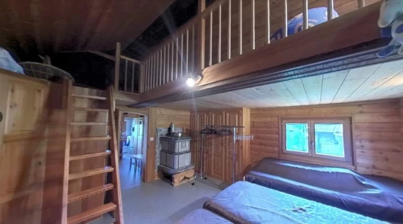 Rustic wooden cabin interior with loft, wood-burning stove, and large windows providing natural light
