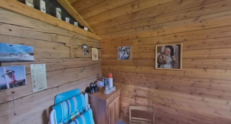 Wooden cabin interior with shelves, framed photos, and a cabinet with various items